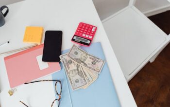 : A desk with a calculator, phone, notepads, glasses, and cash, highlighting the importance of post-move finance habits for managing money
